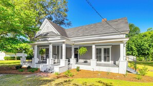 A two-story house with a covered porch, a front yard with landscaping, and a clear blue sky. - Charming Georgia Cottage ~ 19 Mi to Statesboro! (Metter)