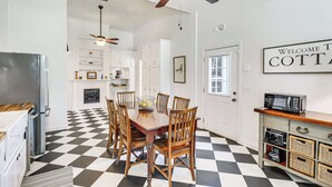 A kitchen with a checkered floor, wooden dining table, and chairs. There is a ceiling fan, a microwave on a wooden cabinet, and a 'Welcome to COTT' sign on the wall. - Charming Georgia Cottage ~ 19 Mi to Statesboro! (Metter)