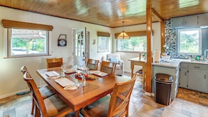 Un coin repas avec une table en bois dressée pour quatre personnes, entourée de chaises, et un espace cuisine comprenant un évier et des placards.