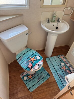 Bathroom features a toilet, sink, and wooden floor with nautical-themed mats.