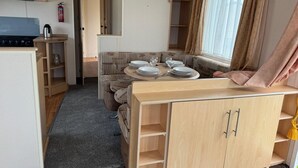 Ett kompakt kök i husbilen med en spis, en diskho och en matplats med ett bord för fyra personer.