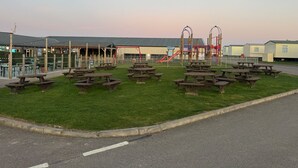 En lekplats med picknickbord och ett överbyggt område, med en byggnad synlig i bakgrunden.