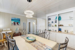 A dining area with a table, chairs, a decorative bowl, and a view of the ocean through a window.