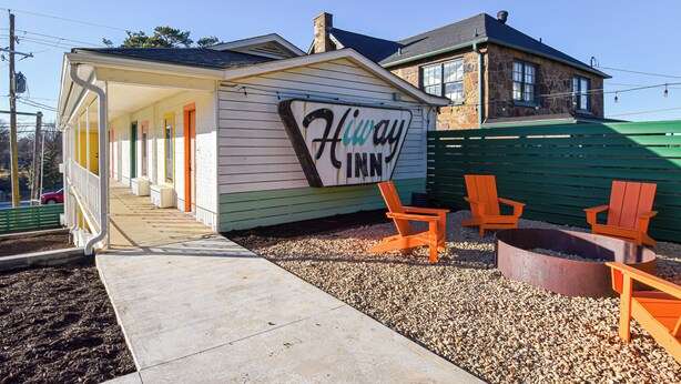 A small, single-story building with a sign reading "Hiway Inn." It features a covered porch with a bench and two orange chairs. - Mid-Century Themed Hotel Room in Fayetteville, AR - The Clementine on College #8 (Fayetteville)