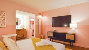 A hotel room with a bed, a bedside table, a mirror, a TV, a dresser, and a bathroom visible through an open door. - Mid-Century Themed Hotel Room in Fayetteville, AR - The Clementine on College #8 (Fayetteville)