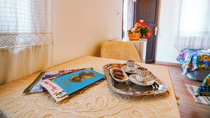 Una bandeja de desayuno ordenada con pasteles y café sobre una mesa, un libro y vistas de una habitación con cama y cortinas.