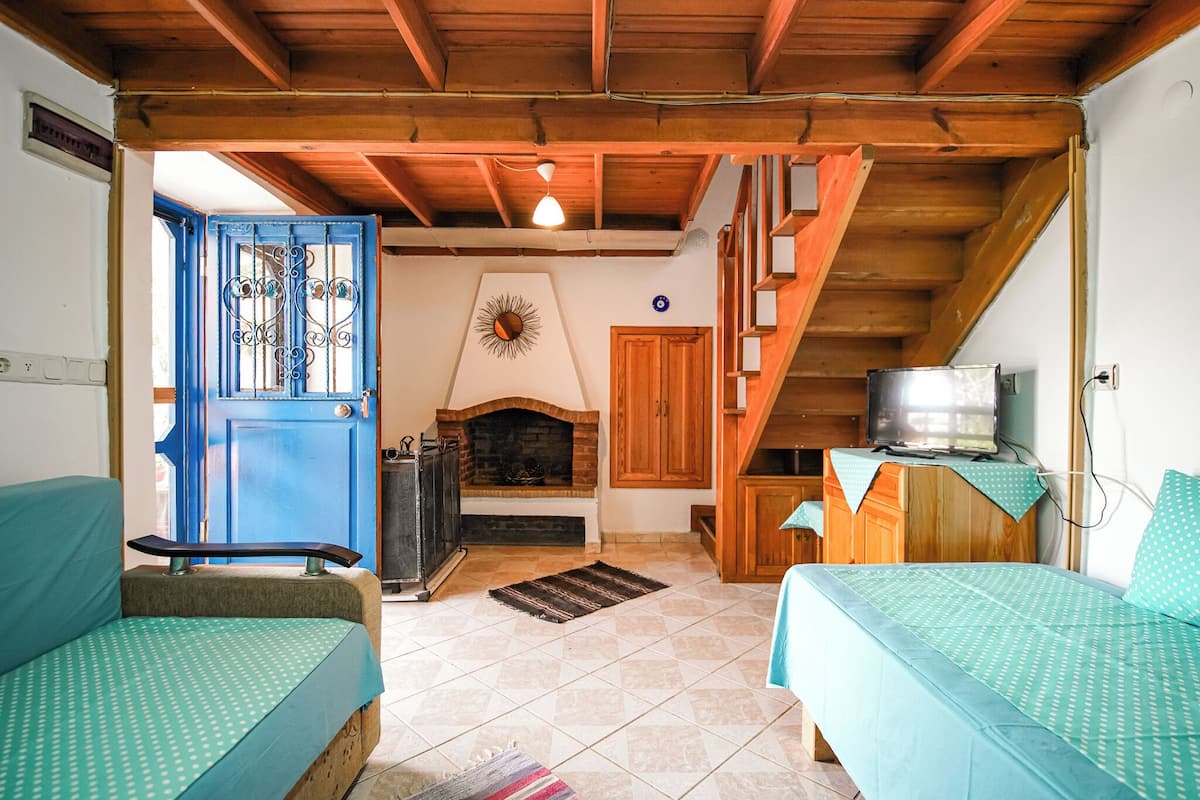 Um quarto aconchegante com lareira, vigas de madeira, uma porta azul e duas camas com roupa de cama combinando.