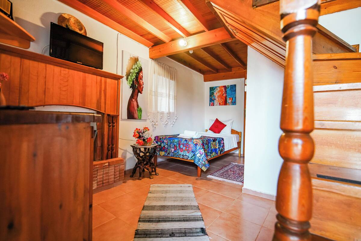 Quarto aconchegante com cama, televisão, armário de madeira e uma pequena mesa com flores.