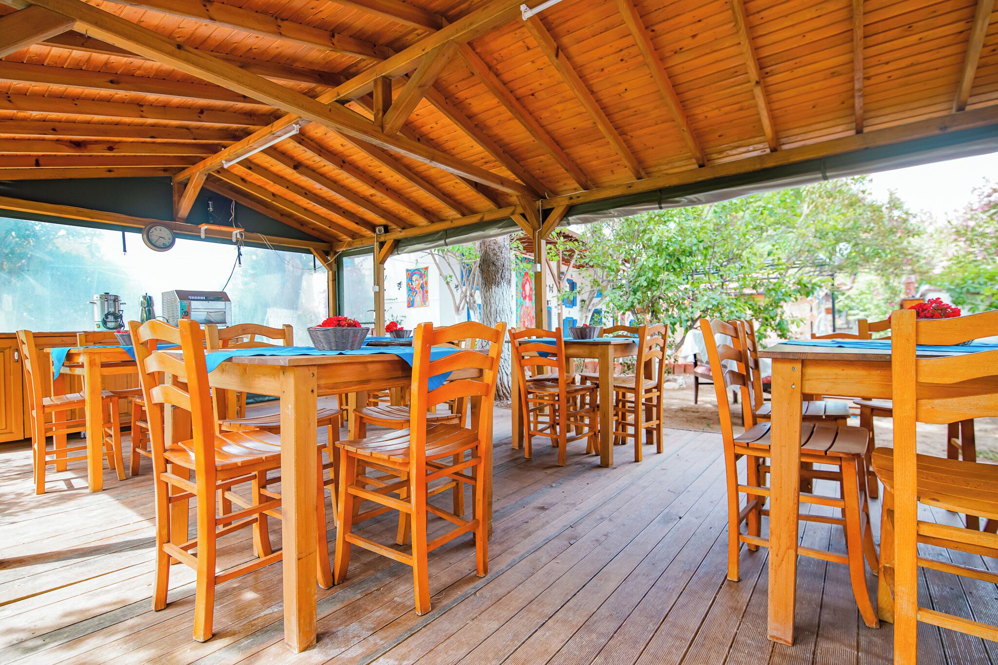 An outdoor wooden deck with multiple tables and chairs, a clock, and a coffee machine.