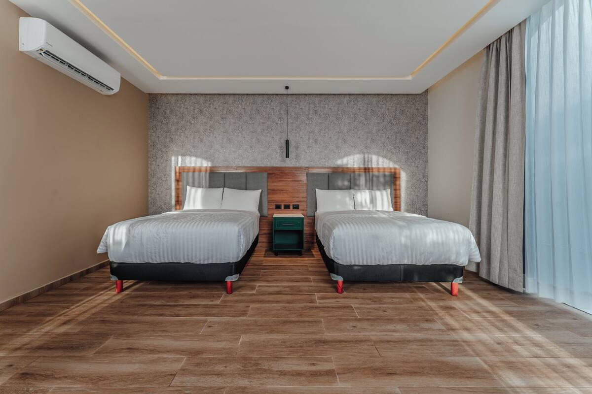 Une chambre d’hôtel moderne avec deux lits, un plancher en bois, un mur à motifs et une grande fenêtre avec des rideaux.