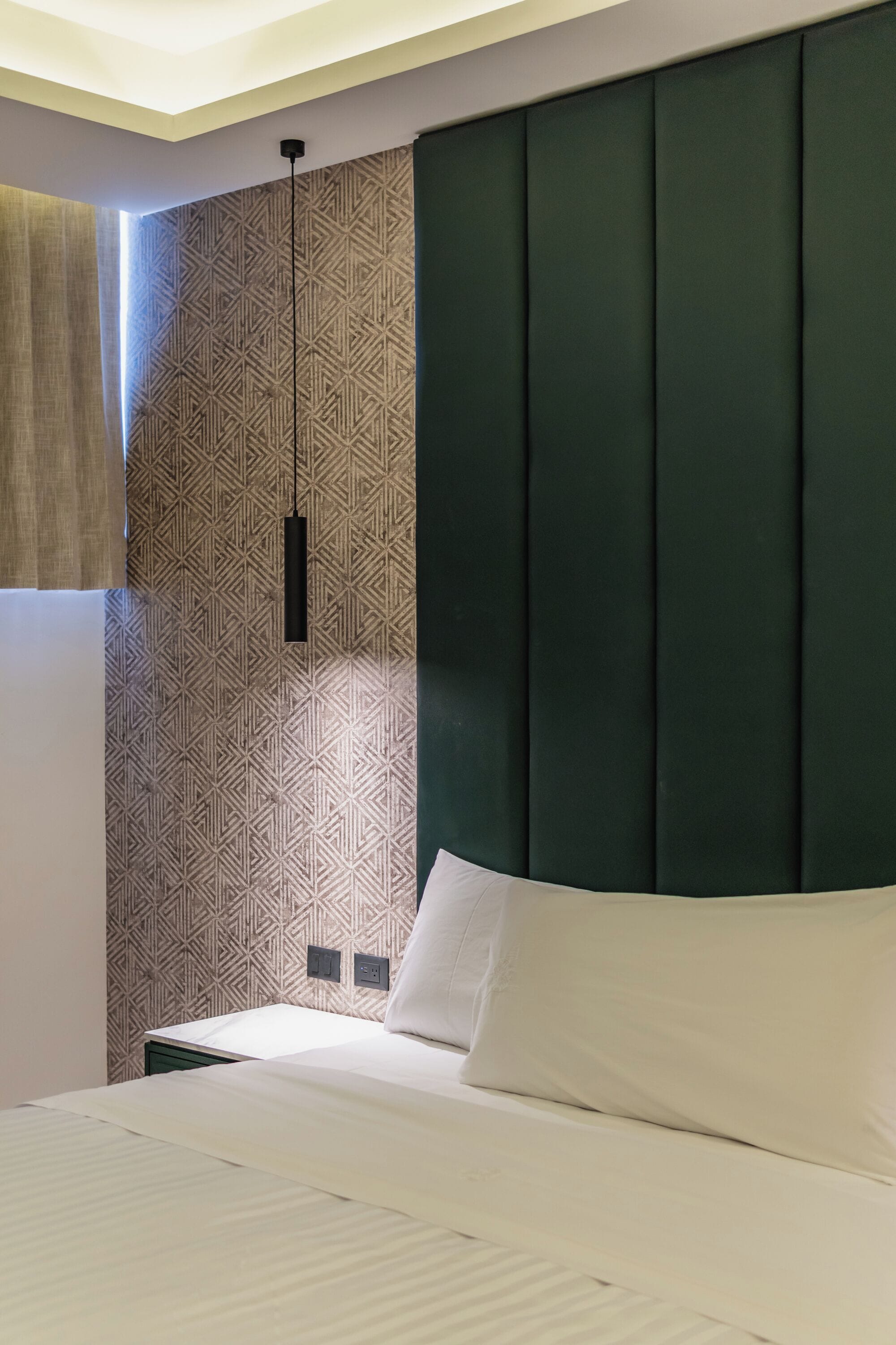 A neatly made bed with white linens, a dark green headboard, and a patterned wall behind it.
