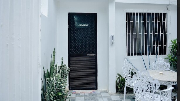 A white exterior with a black door and window bars, a small outdoor seating area with a table and chairs, and some potted plants. - Ocean View Paradise in Puerto Galera (Puerto Galera)