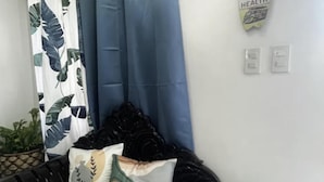 A room with a black sofa, a patterned curtain, a wall sign, and a potted plant. - Ocean View Paradise in Puerto Galera (Puerto Galera)