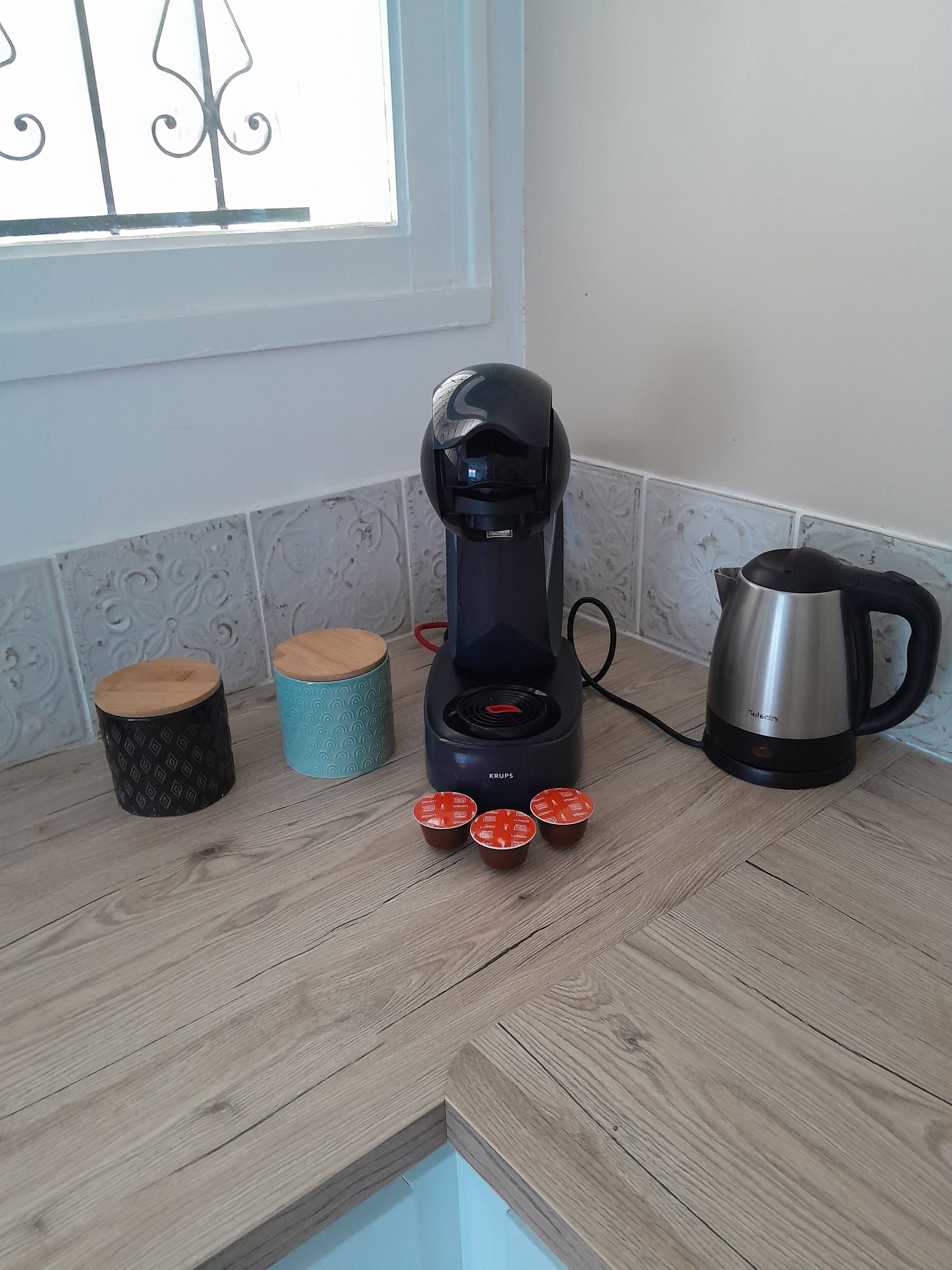 A kitchen with a coffee maker, a kettle, and three small containers on the counter.