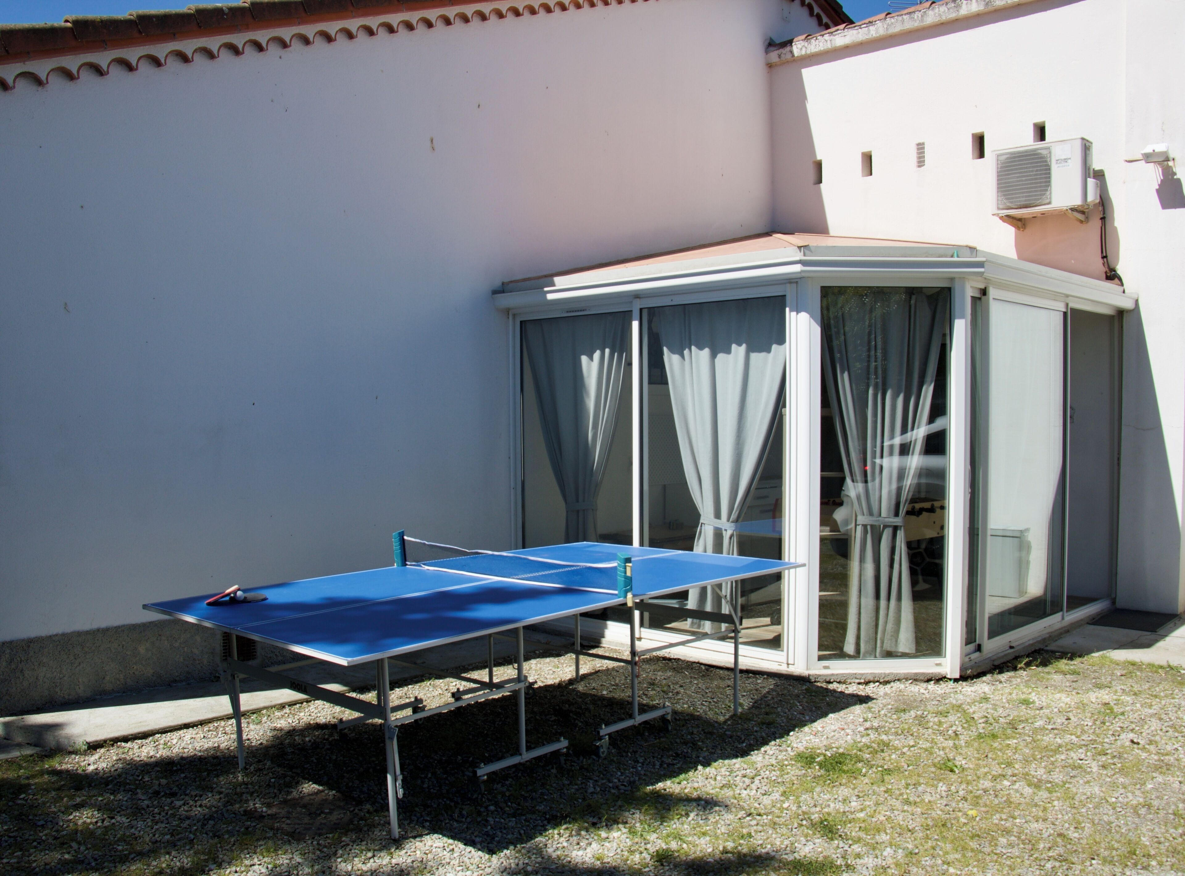 Ein Tischtennis-Tisch steht im Freien neben einem mit Vorhängen ausgestatteten Glasraum.