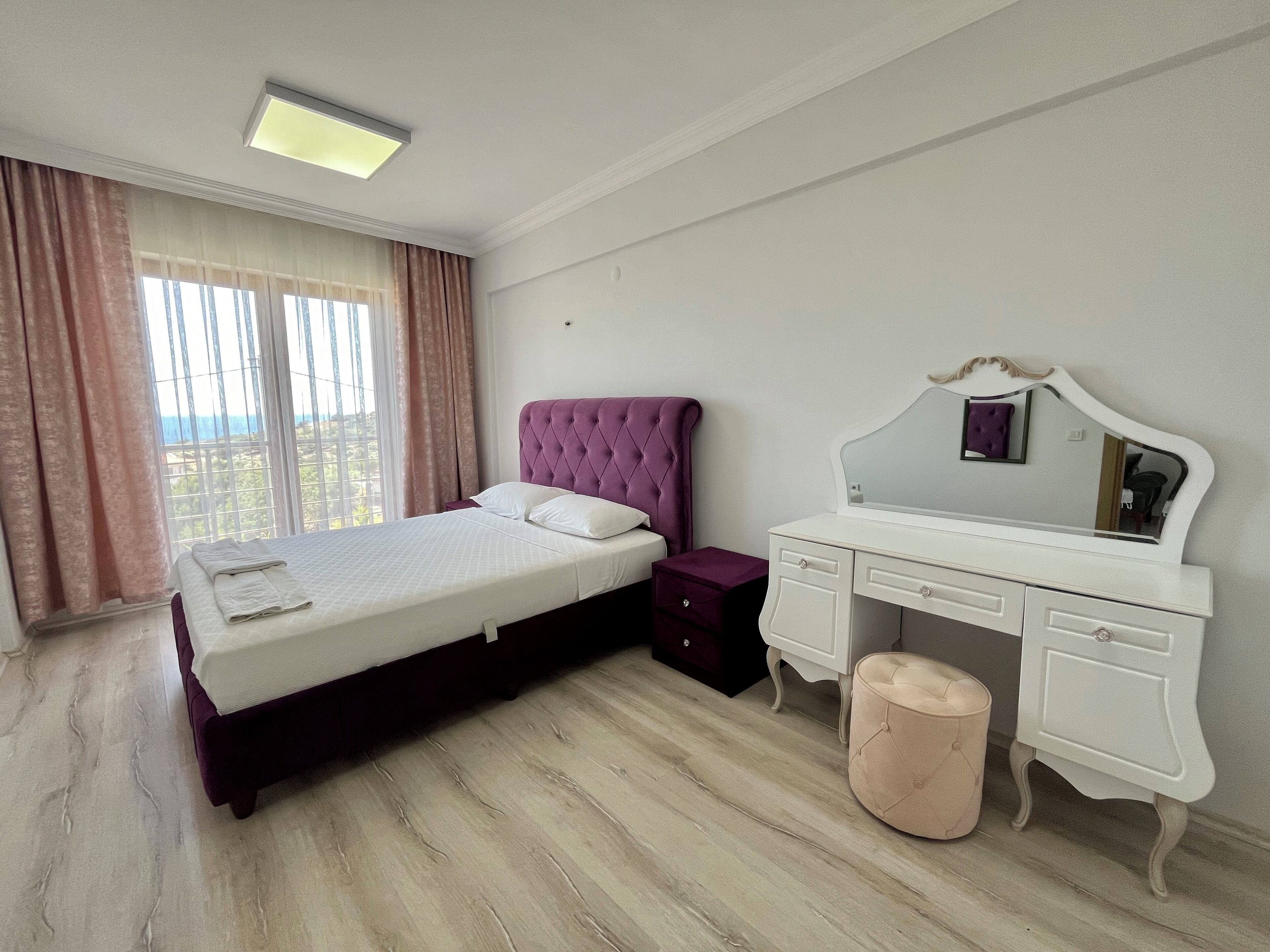 A bedroom with a bed, a dresser, a mirror, and a window with curtains.