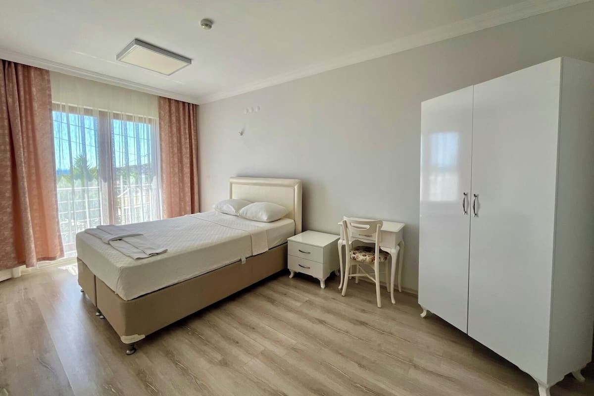 A bedroom with a bed, bedside table, chair, wardrobe, and a window with curtains.