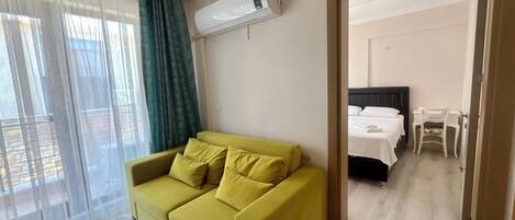 A room with a yellow sofa, a bed with white bedding, and a mirror reflecting the room.
