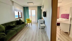 Een moderne woonkamer met een groene bank, een gele fauteuil, een witte bijzettafel en een bed met een roze hoofdeinde.