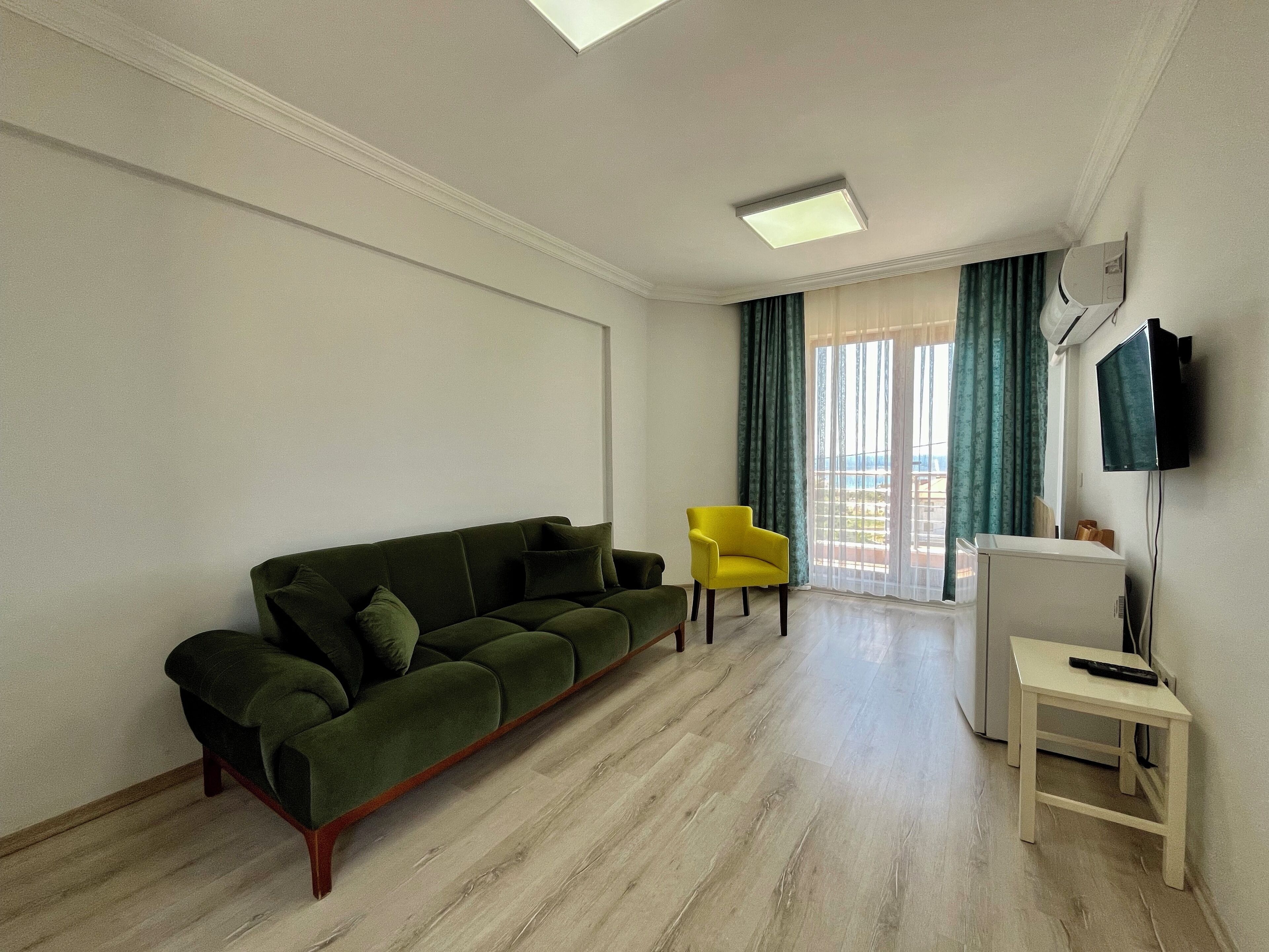 Una sala de estar con un sofá verde, un sillón amarillo, una mesa blanca y un televisor montado en la pared.