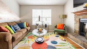 A cozy living room with a brown sofa, colorful cushions, a glass coffee table, and a vibrant rug. - Spacious Douglasville/Lithia Springs Retreat: 5BR, 3BA for Families or Business (Lithia Springs)
