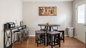 A dining area with a round table and four stools, a painting on the wall, and a window with blinds. - Spacious Douglasville/Lithia Springs Retreat: 5BR, 3BA for Families or Business (Lithia Springs)