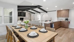 Een moderne keuken met houten kastjes, een centraal eiland en een eetgedeelte met een houten tafel voor vier personen.