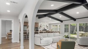 Een ruime woonkamer met een grote witte bank, een groene fauteuil en een kamerkleed met een patroon.