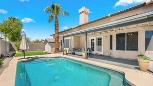 Una piscina con zona de patio, área de estar techada y una palmera.
