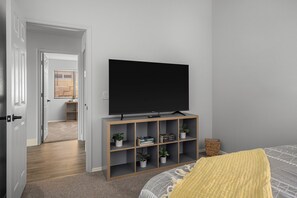 Une chambre avec un grand téléviseur à écran plat posé sur un meuble en bois, un lit recouvert d’une couverture jaune et une petite plante sur le meuble.