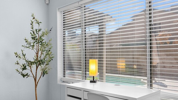 A modern office space with a white desk, a potted plant, and a window with blinds. - Spacious Retreat w/ Free Heated Pool – Close to Stadium & Ballparks! (Peoria)