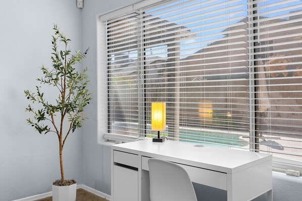 A modern office space with a white desk, a potted plant, and a window with blinds. - Spacious Retreat w/ Free Heated Pool – Close to Stadium & Ballparks! (Peoria)