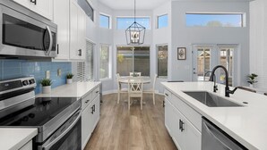 A modern kitchen with white cabinetry, a black stove, and a large island with a sink. - Spacious Retreat w/ Free Heated Pool – Close to Stadium & Ballparks! (Peoria)