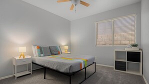 A bedroom with a bed, nightstands, a ceiling fan, a window with blinds, and a small shelf unit. - Spacious Retreat w/ Free Heated Pool – Close to Stadium & Ballparks! (Peoria)