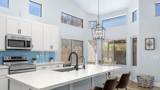 Una cocina moderna con armarios blancos, una isla grande, electrodomésticos de acero inoxidable y una lámpara colgante.