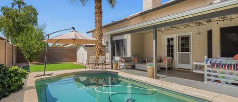 A residential backyard with a swimming pool, patio furniture, and a covered outdoor seating area.