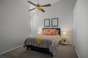 A bedroom with a bed, a ceiling fan, two wall-mounted picture frames, a bedside table with a lamp, and a window with blinds. - Spacious Retreat w/ Free Heated Pool – Close to Stadium & Ballparks! (Peoria)