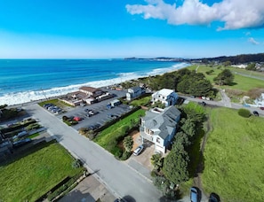 Vue aérienne d’un quartier résidentiel situé sur la côte, avec des maisons, un parking et une route menant à la plage.
