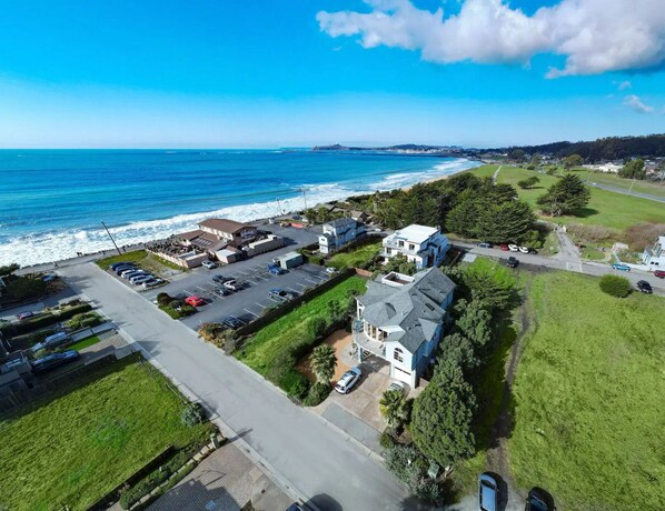 An aerial view of a coastal residential area with houses, a parking lot, and a road leading to the beach.