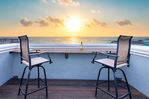 Een balkon met twee stoelen gericht op een zonsondergang boven de oceaan.