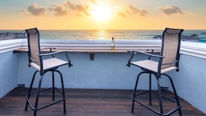 Un balcon avec deux chaises donnant sur un coucher de soleil sur l’océan.