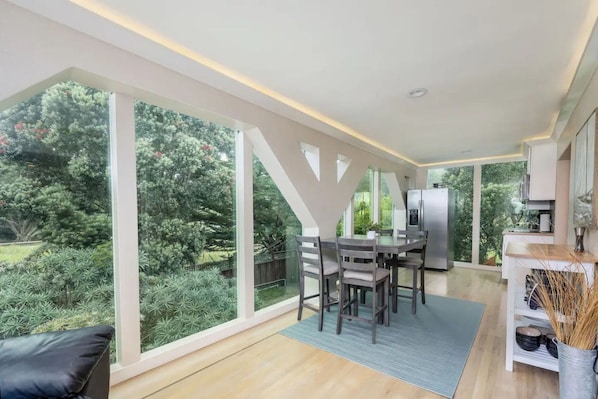 A modern kitchen with a large island, a dining area with a table and chairs, and a view of a lush garden through large windows.