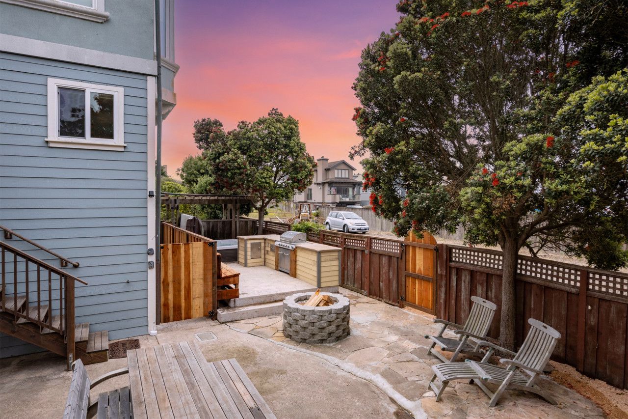 A backyard with a fire pit, outdoor seating, and a wooden deck.