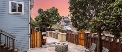 A backyard with a fire pit, outdoor seating, and a wooden deck.