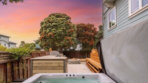 A backyard with a hot tub, wooden deck, and a large tree. - Seaside Escape: 1 block to Beach, Private Hot Tub, Fire Pit & BBQ (El Granada)