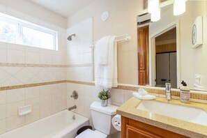 Une salle de bain avec une baignoire, des toilettes et un lavabo. Il y a une fenêtre au-dessus de la baignoire et un miroir au-dessus du lavabo.