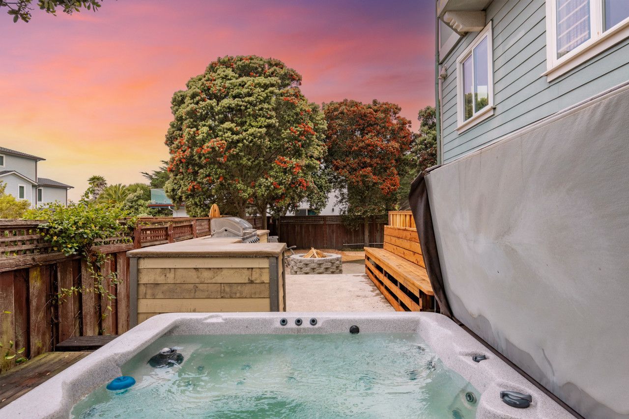 Patio trasero con jacuzzi, terraza de madera y un gran árbol.