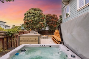 A backyard with a hot tub, wooden deck, and a large tree. - Seaside Escape: 1 block to Beach, Private Hot Tub, Fire Pit & BBQ (El Granada)