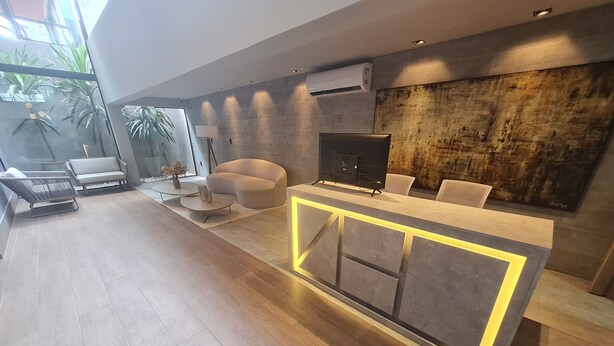 A modern living area with a sofa, a coffee table, and a TV. There is a wooden floor and a large window with plants. - URBAN TAMBAU Flat by Penareia.tur.br (João Pessoa)