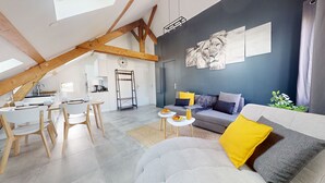 A modern loft-style living space with a dining area, a sofa with a yellow pillow, and artwork on the walls.